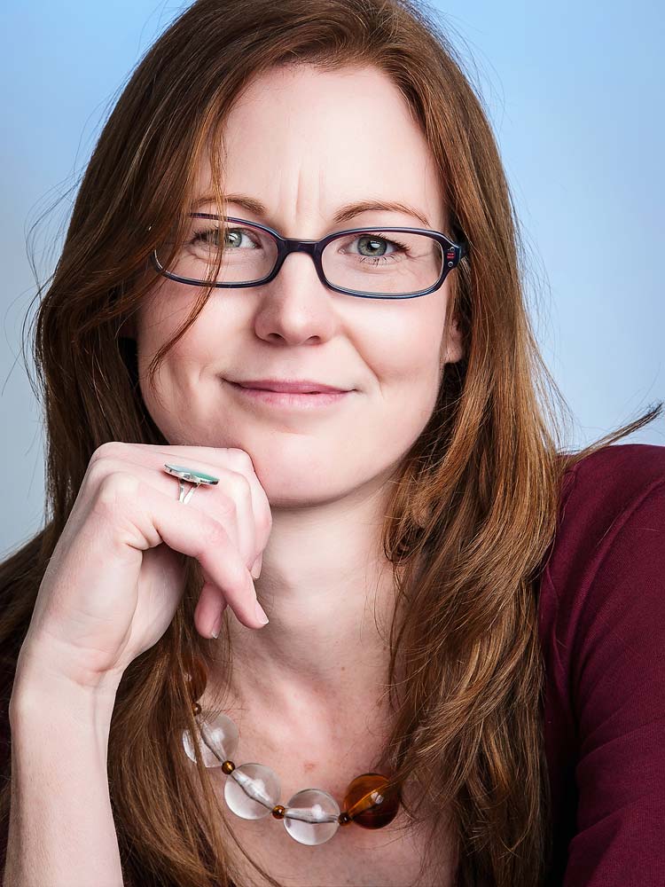Contact Sussex Headshots. Elegant Sussex headshot of a confident woman with red hair and glasses, showcasing professional portrait photography services in Sussex.